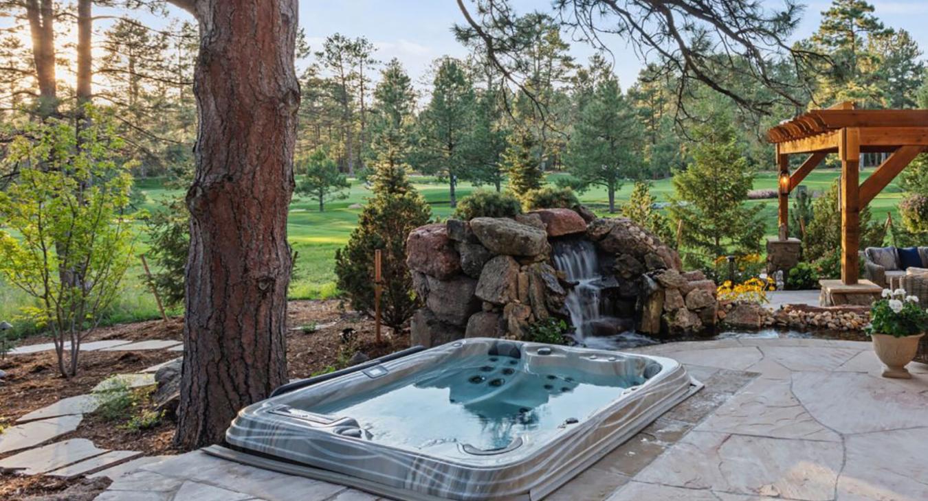 Hot tub installed outdoors near a landscaped golf course with trees and natural stone features.