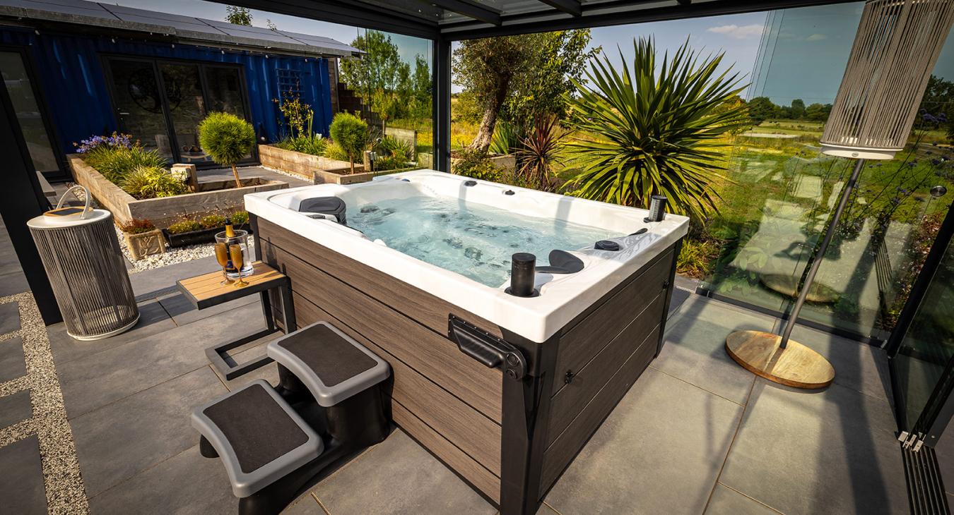 Modern hot tub installed on a patio under a covered outdoor living space with surrounding landscaping.